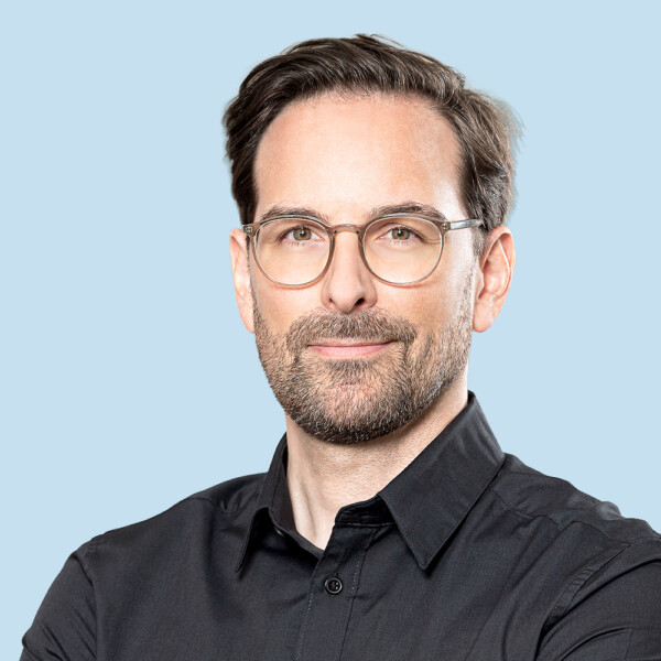 Ein Mann mit Bart und Brille, der ein schwarzes Hemd mit Knöpfen trägt.