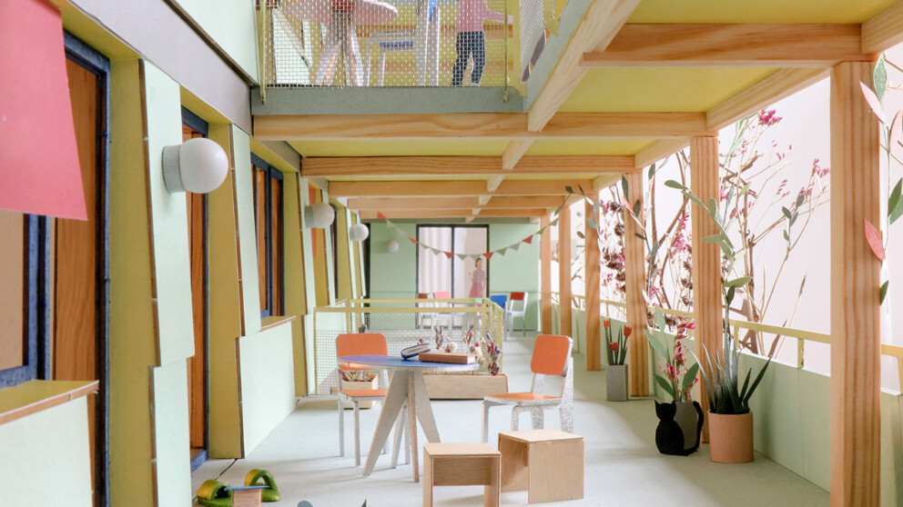 Ein farbenfroher, moderner Wohnungsbalkon mit Tischen, Stühlen, Pflanzen und Kinderspielzeug. Auf beiden Ebenen sind Menschen zu sehen, von denen einer im Obergeschoss steht.
