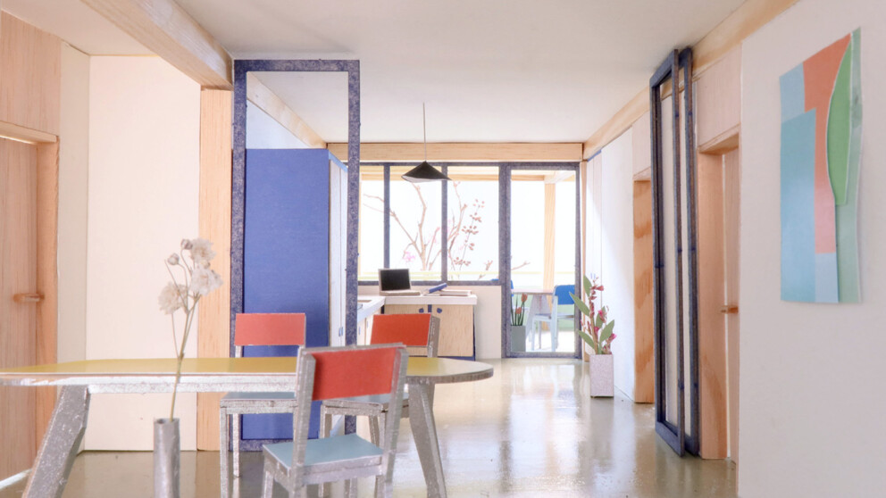 Heller, moderner Essbereich mit bunten Stühlen, einem runden Tisch, Pflanzen und abstrakter Wandkunst. Große Fenster lassen Tageslicht herein.