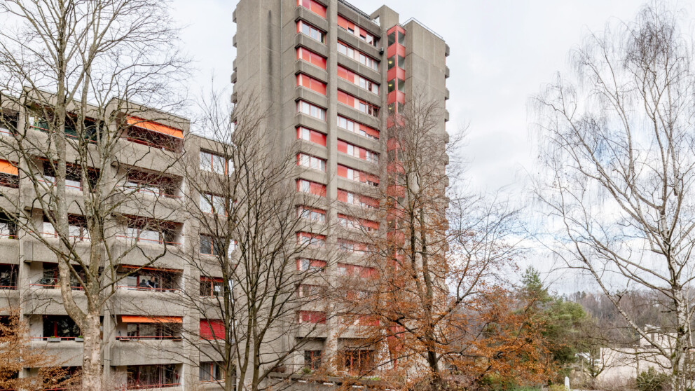 Hohe Betonwohnblocks mit orangefarbenen Balkonmarkisen, eingerahmt von kahlen Bäumen.