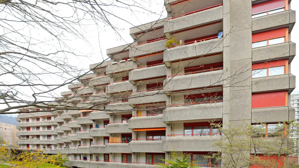 Ein großes, stufenförmig angelegtes Wohnhochhaus aus Beton mit roten Balkonen und Fensterläden.